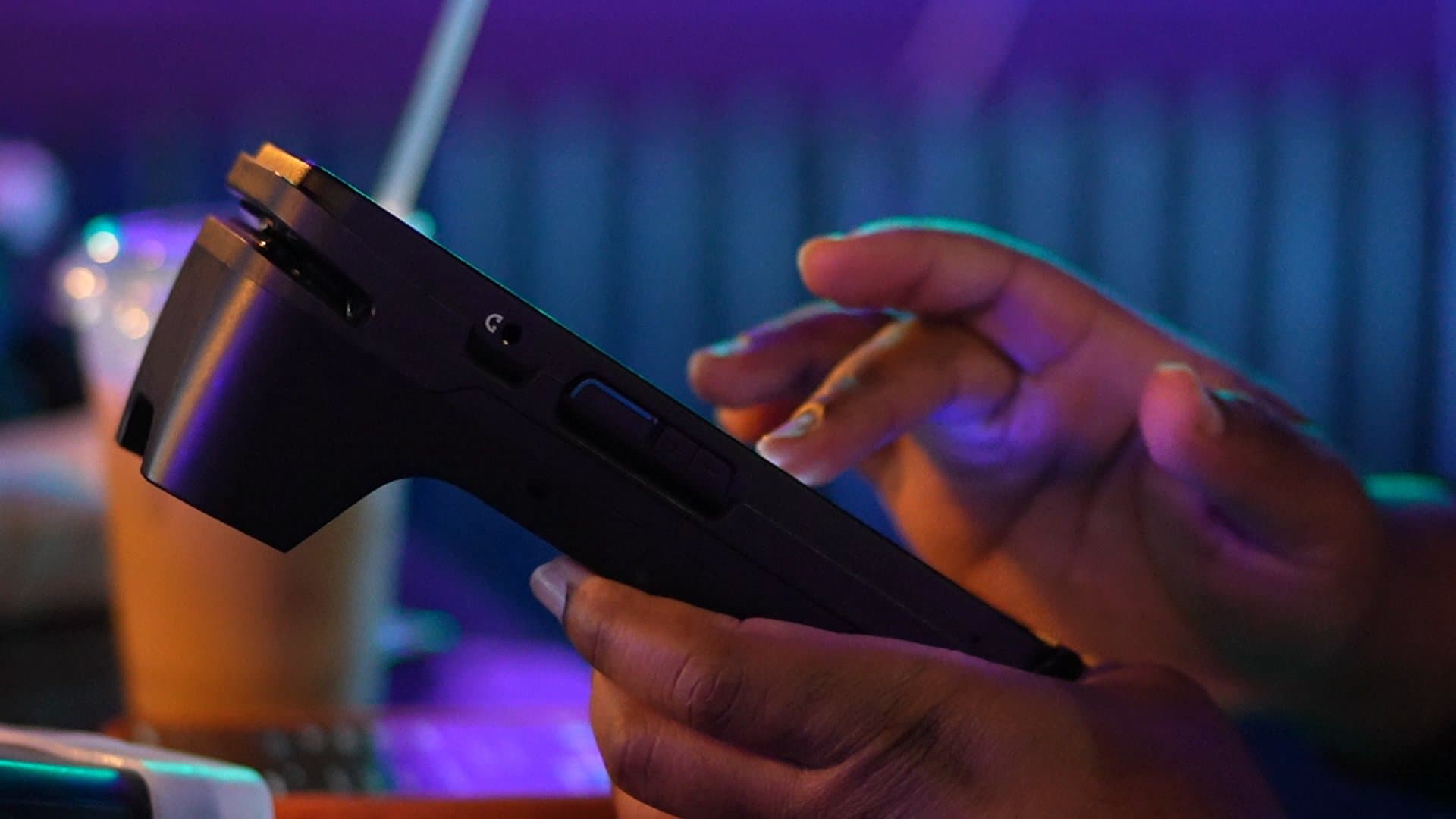 A hand passes the card reader across the bar under neon light
